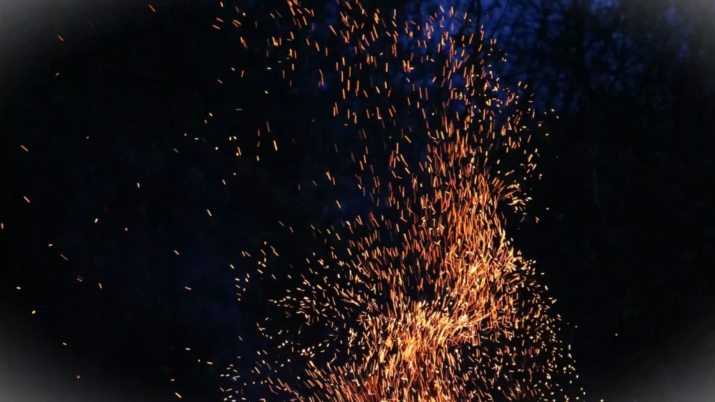 Orange fire sparks rising against a dark night background with glowing ember trails.